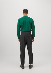 Camisa verde de manga larga con cuello a rayas, combinada con pantalones negros ajustados con cremalleras laterales y zapatos negros.
