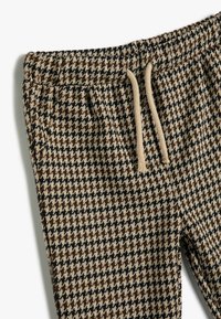 Bruine en beige hounds-tooth patroon joggers met een elastische tailleband en een beige trekkoord, met een zachte stoftextuur.