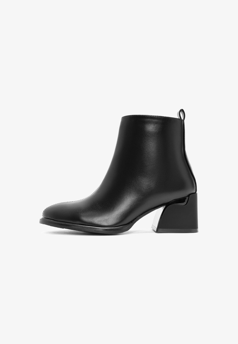 Zwarte leren enkelboot met een ronde neus en een metalen accent op een chunky hak. Voorzien van een trekloop achteraan voor gemakkelijk aan- en uittrekken.