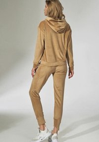 Beige velours trainingspak met capuchon, voorzien van een ontspannen pasvorm, manchet mouwen en broeken, en gecombineerd met witte sportschoenen.