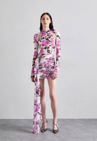 Robe mini florale blanche, ornée de motifs de roses roses et marron, à manches longues, avec des découpes et un drapé latéral fluide.