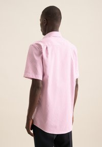 Camicetta a maniche corte con righe rosa e bianche, caratterizzata da un colletto standard, yoke posteriore e orlo curvo. Realizzata in tessuto leggero.