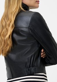 Zwarte leren jas met een aansluitend ontwerp, hoge kraag en geribde zoom. Beschikt over een gladde textuur en gedetailleerde stiksels op de schouders.