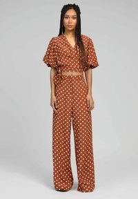 Ensemble en deux pièces à pois de couleur brun rouillé, comprenant un haut crop à enrouler avec des manches bouffantes et un pantalon ample avec une fermeture à bouton.