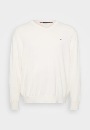 Kreem V-kaelusega sviiter, mis on valmistatud pehmest kangast, pika varrukaga ja soonikuotsi, väikese logoga vasakul rinnal.