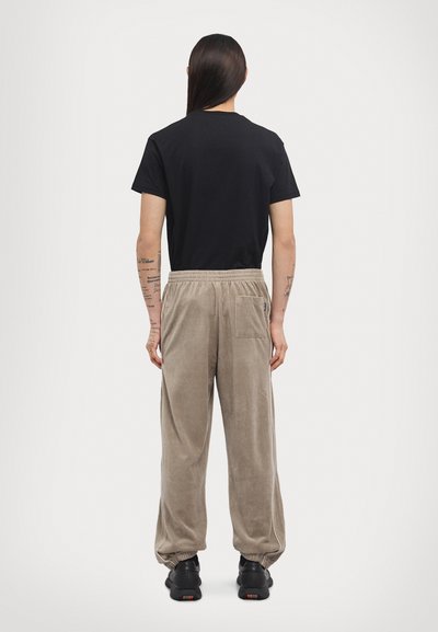 Black cotton t-shirt paired with beige corduroy sweatpants featuring a side pocket, elastic cuffs, and matching waistband. Black sneakers complete the look.