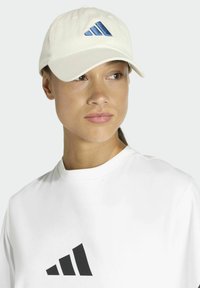Gorra de béisbol blanca con tres rayas azules en la parte delantera. La tela parece suave y la visera se curva hacia abajo.