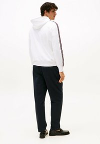 Sudadera blanca con capucha y cordón, con rayas laterales en rojo y azul marino, combinada con pantalones azul marino y mocasines negros. Tejido suave y casual.
