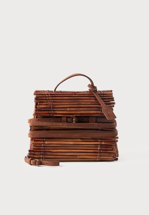 Sac à main rectangulaire en bambou marron avec des lanières en cuir, une poignée supérieure et une étiquette bagage sur un fond clair uni.