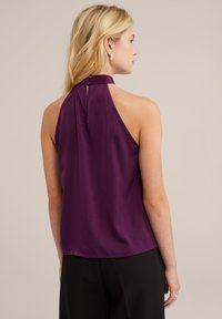 Fialový top s halter výstřihem a hladkou texturou, se zapínáním na knoflík na zádech a volným střihem, v kombinaci s černými kalhotami.