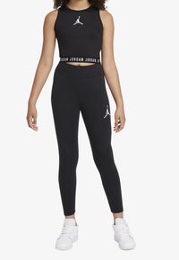 Czarny sportowy crop top i legginsy z białym logo Jordana. Elastyczny materiał, dopasowany krój. Akcentowany pas z powtarzającą się nazwą marki.