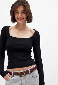 Schwarzes, geripptes Langarmoberteil mit einem quadratischen Ausschnitt, kombiniert mit hellgrauen Jeans und einem kastanienbraunen Gürtel mit einer goldenen runden Schnalle.