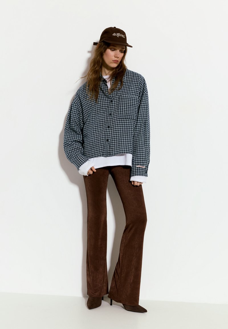 Camicia button-up a quadri blu e bianchi di grandi dimensioni, indossata sopra un top bianco, abbinata a pantaloni a zampa d'elefante marroni e tacchi a punta marroni.