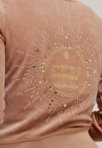 Felpa in velluto bronzo con un design circolare scintillante che presenta la scritta "JUICY COUTURE" in giallo, arricchita da strass e decorazioni in perline.