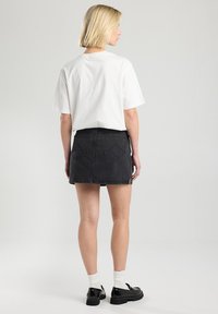 Falda de mezclilla negra con dobladillo deshilachado, dos bolsillos traseros y un ajuste relajado, combinada con una camiseta blanca básica y calzado negro.