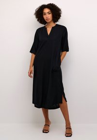 Black midi dress with a V-neckline, short sleeves, side slits, and pocket detail. Made from a smooth, lightweight fabric.