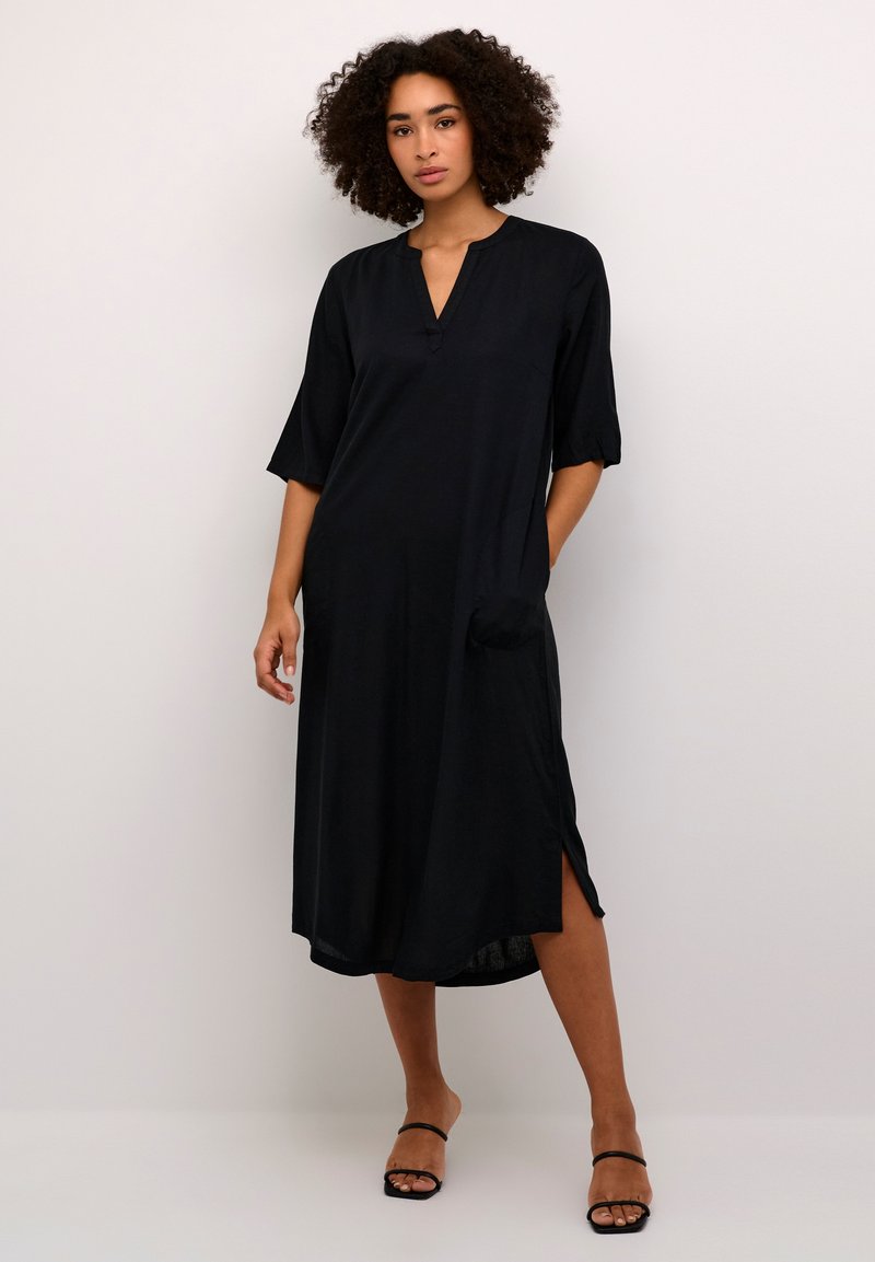 Black midi dress with a V-neckline, short sleeves, side slits, and pocket detail. Made from a smooth, lightweight fabric.