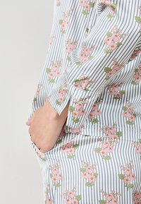 Camisa de algodón con estampado floral en rayas azules y blancas. Cuenta con mangas acampanadas y un bolsillo lateral con un sutil detalle de abertura.
