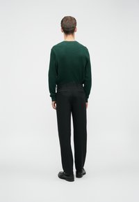 Groene geribbelde trui gecombineerd met zwarte broek, met een ontspannen pasvorm en een gladde textuur. Eenvoudig ontwerp zonder zichtbare patronen of accenten.