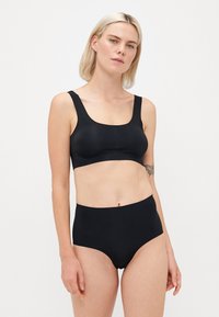 Svart sømløs bralette med brede stropper og firkantet halslinning, kombinert med høytsittende svart undertøy. Glatt tekstur, minimalistisk design.