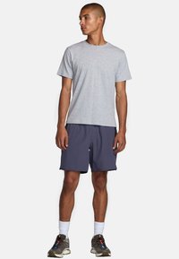T-shirt en coton gris porté avec un short marine, tous deux avec une coupe décontractée. Les chaussures sont sombres avec des accents colorés et les chaussettes sont blanches.