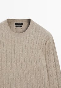 Béžový svetr se vzorem copů, vyrobený ze 100% bavlny. Má klasický kulatý výstřih a texturovaný vzor po celé látce.