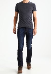 Dunkelgraues T-Shirt mit kurzen Ärmeln und Tasche, kombiniert mit enganliegenden blauen Jeans und braunen Stiefeln. Das Outfit hat einen lässigen, modernen Schnitt.