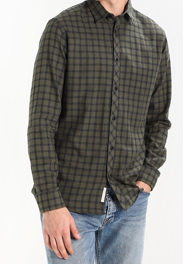 Chemise en flanelle à carreaux verts et noirs avec un col boutonné et des manches longues. Le tissu a une texture douce. Dispose d'une étiquette latérale.
