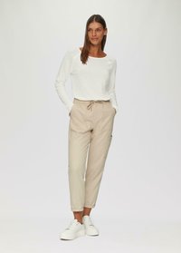 Pantalons de jogging beige avec taille élastique et cordon de serrage, dotés de poches latérales ; associés à un simple t-shirt blanc à manches longues et des baskets blanches.