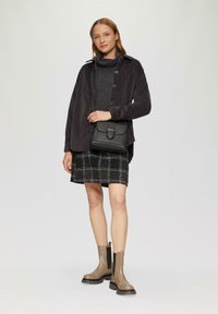 Zwarte button-up cordjasje over een donkere gebreide trui, geruite zwart-witte rok en taupe enkellaarzen met dikke zolen. Zwarte crossbody tas.