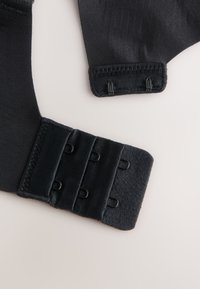 Suport pentru încheietura mâinii din material textil negru, cu închidere reglabilă cu velcro și cârlige metalice pentru fixare sigură pe suprafețe deschise la culoare.
