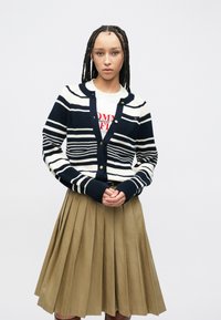 Μπλε ναυτικό και εκρού ριγέ ζακέτα με κουμπιά, σε συνδυασμό με μια πλισέ χακί φούστα. Υλικό από βαμβακερό μείγμα, με ριμπ μανσέτες και τελείωμα στη μέση.