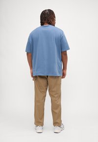 T-shirt bleu clair à manches courtes associé à un pantalon cargo beige, présentant une coupe décontractée et des poches arrière. Chaussures décontractées visibles.