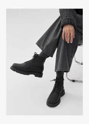 Mustad mustad nahast ankle'd, millel on nöörimisfront ja külgkeetmine, pakuvad paksut kummist tallat ja siledat viimistlust. Kanna tumesiniste laia pükse.