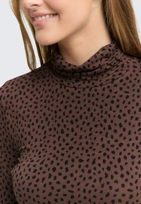 Brauner Rollkragenpullover aus weichem, elastischem Material, mit einem schwarzen unregelmäßigen Punktmuster. Enganliegendes Design mit hohem Kragen.