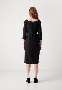 Abito nero con una silhouette aderente, maniche a tre quarti e scollo rotondo. Presenta una zip sul retro discreta e una texture liscia.