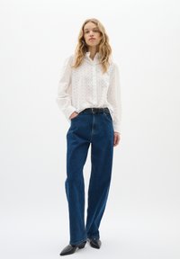 Camicia bianca con texture a occhio, abbinata a jeans a gamba dritta in denim blu scuro a vita alta e scarpe nere con punta a punta.