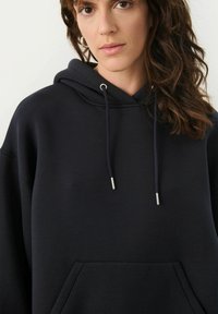 Svart oversized hoodie med snörning och silverfärgade toggles, med en framficka i känguru-stil och ett mjukt, texturerat tyg.