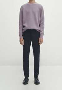 Pull tricoté texturé violet clair associé à un pantalon bleu marine foncé et des chaussures à lacets noires, présentant une tenue simple et moderne.