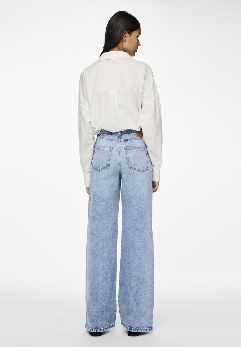 Lichtbeige, langemouw shirt gecombineerd met lichtblauwe, wijdvallende jeans. De jeans hebben een klassiek vijf-pocket ontwerp en een vervaagde afwerking.