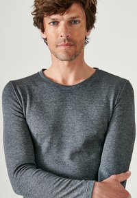 Grijze langslavige shirt van textuurstof. Klassieke ronde hals met subtiele stikdetails. Fitted ontwerp, gladde afwerking en rekbaar materiaal.