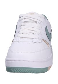 Bílé tenisky s hladkým koženým svrškem, s mátově zeleným logem Nike a akcenty, texturovanou gumovou podrážkou a zaobleným tvarem špičky.