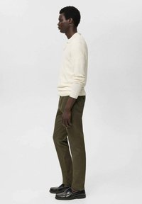 Cream ribbed long-sleeve polo shirt paired with olive green trousers. Black loafers complete the outfit. Focus on clean lines and neutral colors.