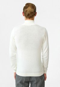 Witte, lichte trui met lange mouwen en een hoge kraag, met een gladde textuur en ribbelzoom, gecombineerd met gestreepte broek.