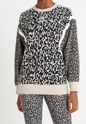 Femme portant un haut à manches longues à motif abstrait noir et blanc et un legging assorti avec des poignets et un col beige clair.