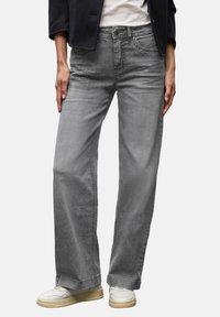 Jeans ampia grigia in un morbido tessuto di denim. Presentano cinque tasche e cuciture tonali. Indossati con sneakers bianche e una giacca nera.