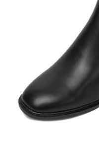 Czarny skórzany botek za kostkę z okrągłym noskiem, gładką fakturą i subtelnymi przeszyciami wzdłuż podeszwy. Posiada trwałą gumową podeszwę.