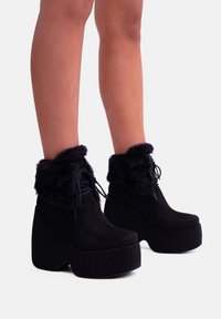 Stivali platform neri con risvolto in ecopelliccia, materiale scamosciato, punta arrotondata e suola spessa. Dettaglio con lacci nella parte anteriore.