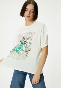 Hvid bomulds oversized t-shirt med farverig grafisk design med frø, sommerfugle og tekst. Korte ærmer og afslappet pasform.