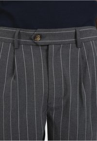 Pantalon gris à fines rayures blanches verticales, taille boutonnée, passants de ceinture et un top bleu marine rentré.